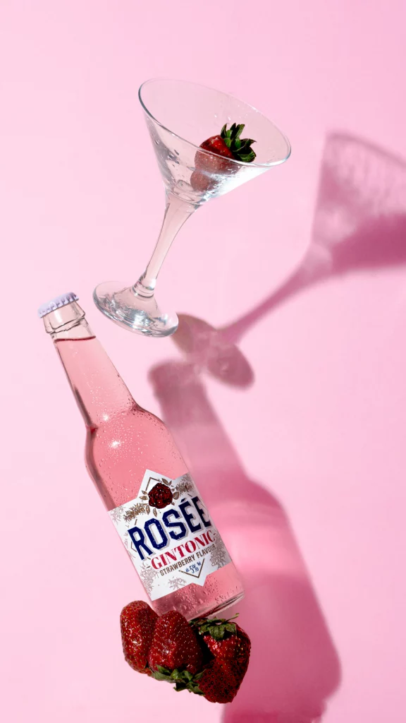 Botella de ginebra con fresas sobre fondo rosa fotografía gastronómica de bebida en valencia foodbyleo